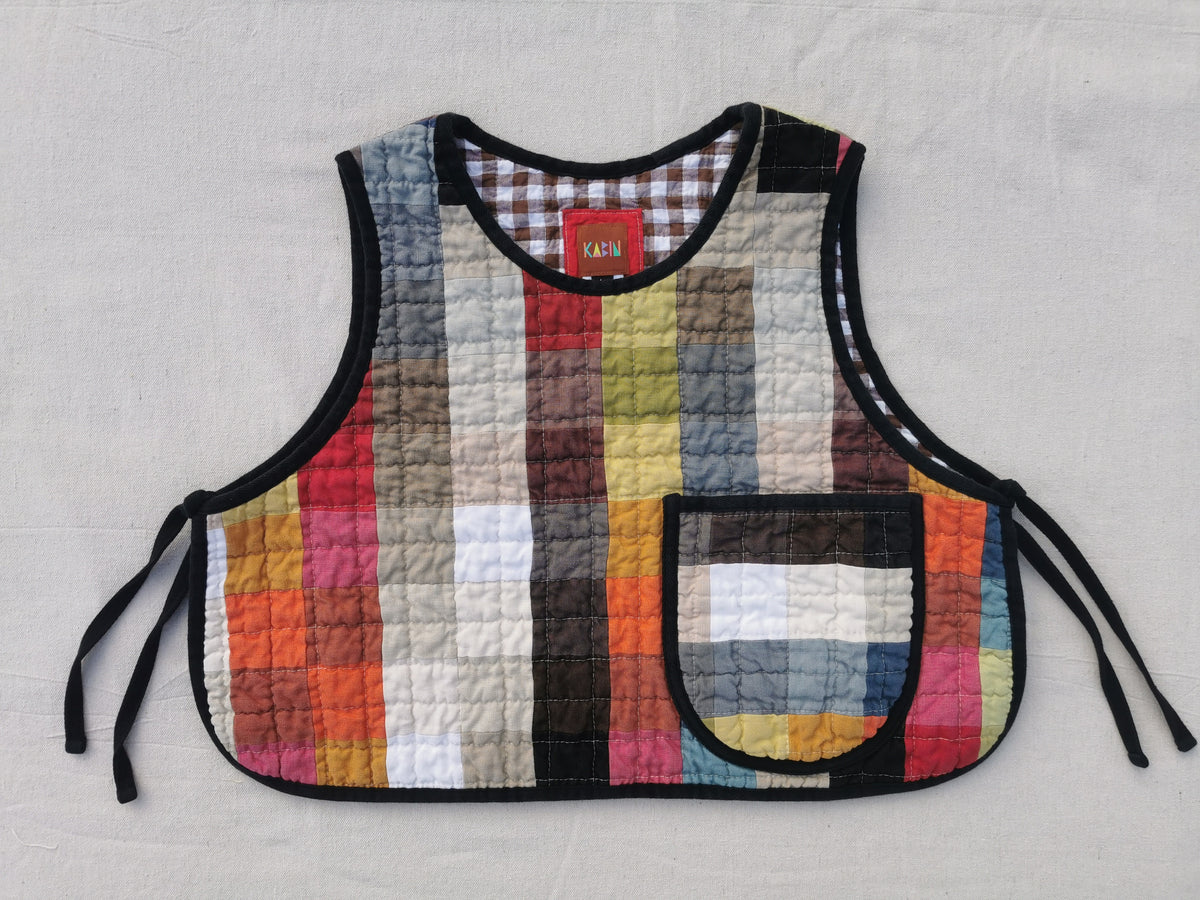 The front of a handmade colourful quilted patchwork linen vest by KABIN NZ with a patch pocket, brown gingham lining and black binding.