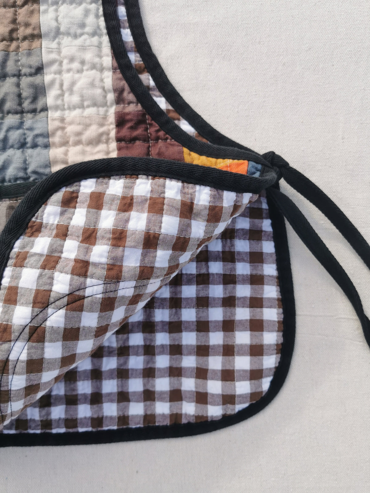 Close-up of the lining of a handmade colourful quilted patchwork linen vest by KABIN NZ with a patch pocket, brown gingham lining and black binding.