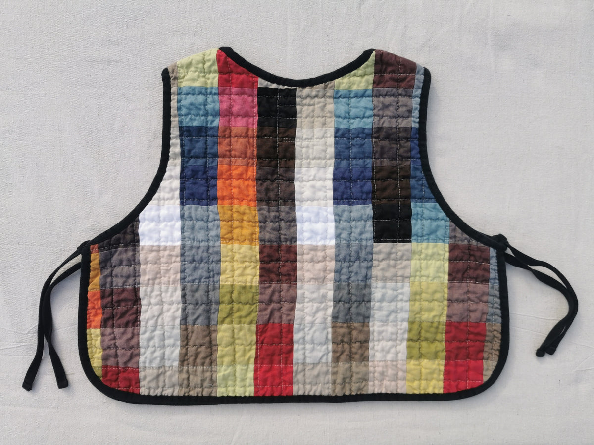 The back of handmade colourful quilted patchwork linen vest by KABIN NZ with a patch pocket, brown gingham lining and black binding.