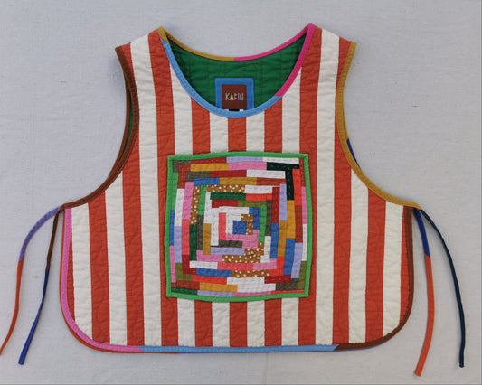 A handmade quilted vest with orange and white vertical stripes, featuring a colorful geometric patchwork design on the front and multicolored binding.