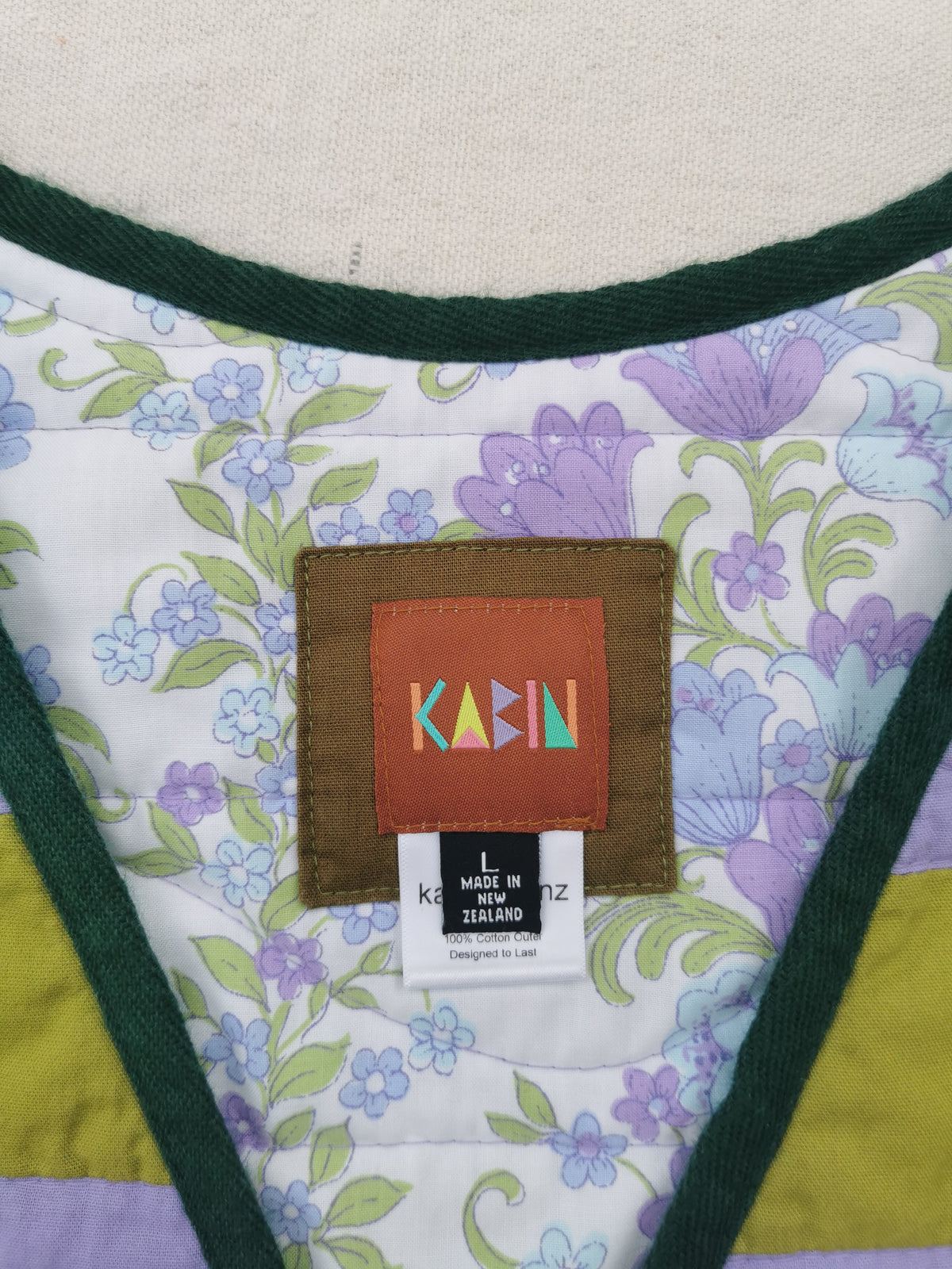 Close-up of a handmade quilted vest by KABIN NZ, showing a floral print lining and dark green trim.