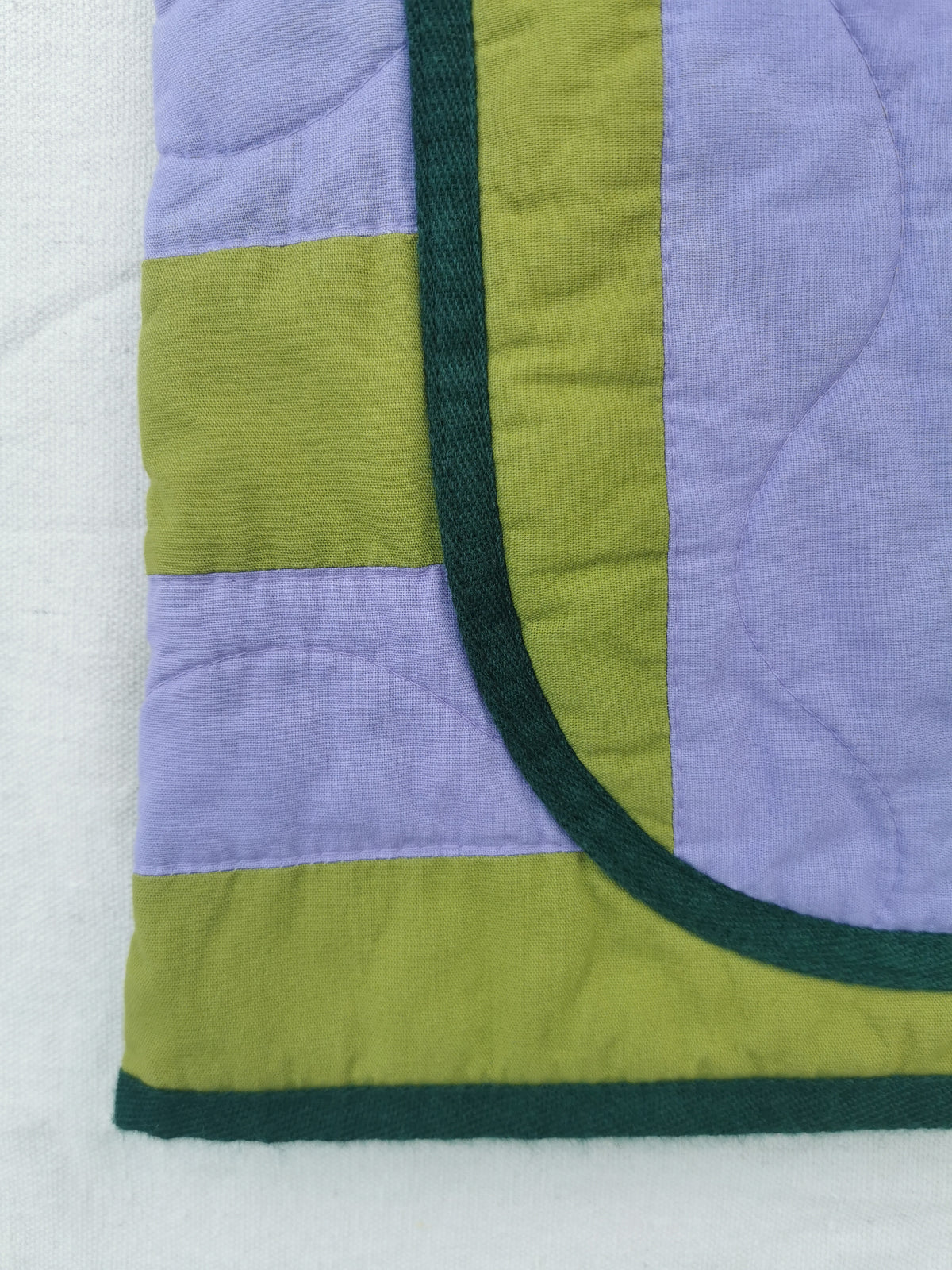 A close-up of a handmade quilted vest by KABIN NZ showing lavender and olive green fabric panels with dark green trim, laid on a white background.