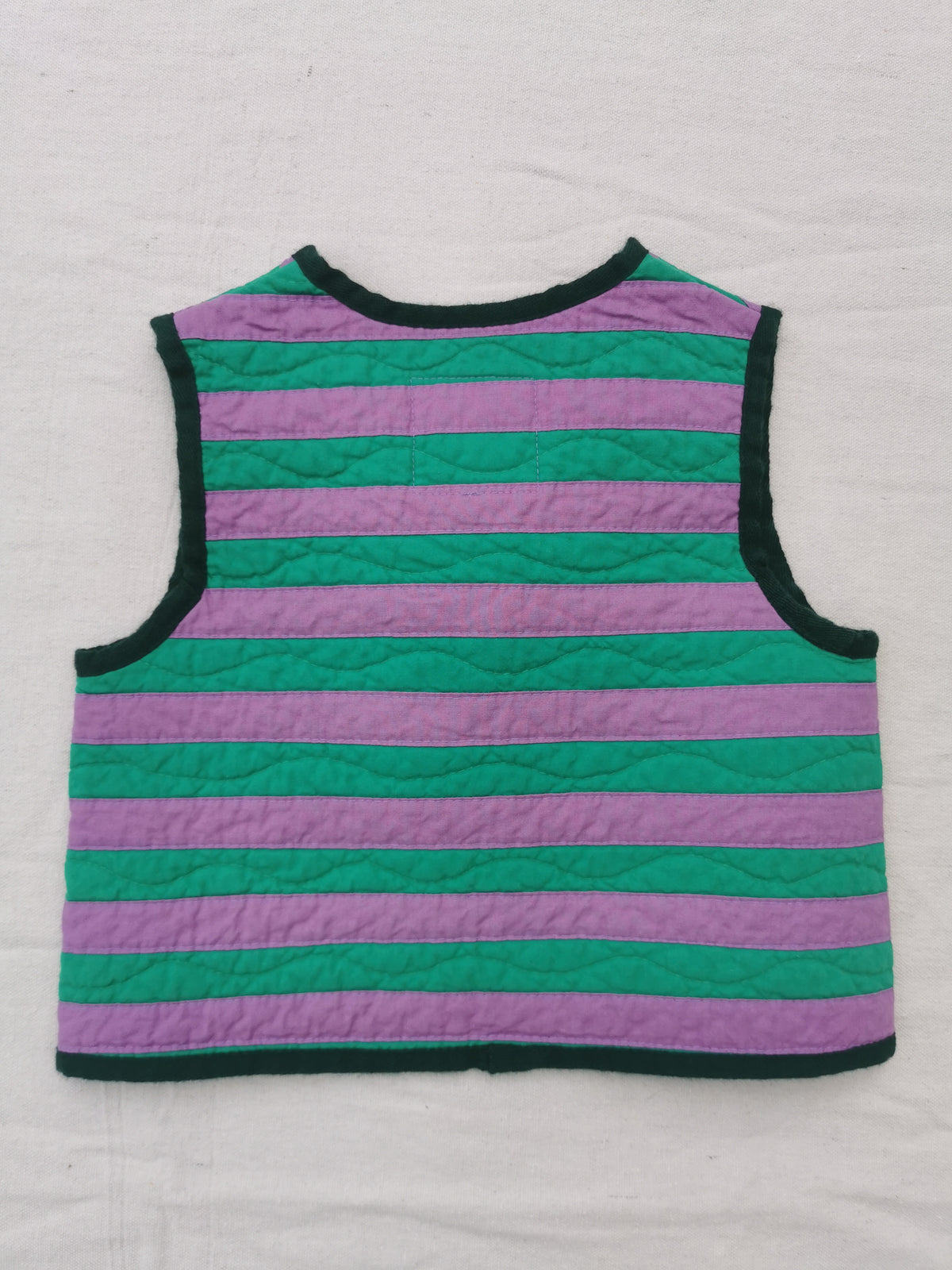 A handmade quilted vest with horizontal purple and green stripes and dark green trim, laid flat on a white fabric background by KABIN NZ.